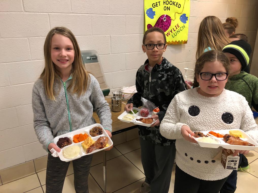 Three children smile with full lunch trays